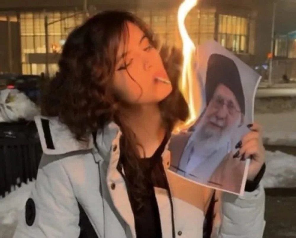 Een demonstrant steekt haar sigaret aan met het brandende portret van de Iraanse dictator Ali Khamenei - X