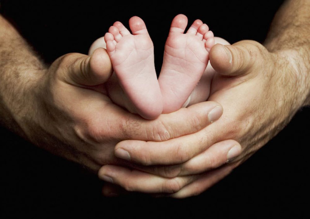A newborn baby¥s feet rest in his father¥s hands against a black background.