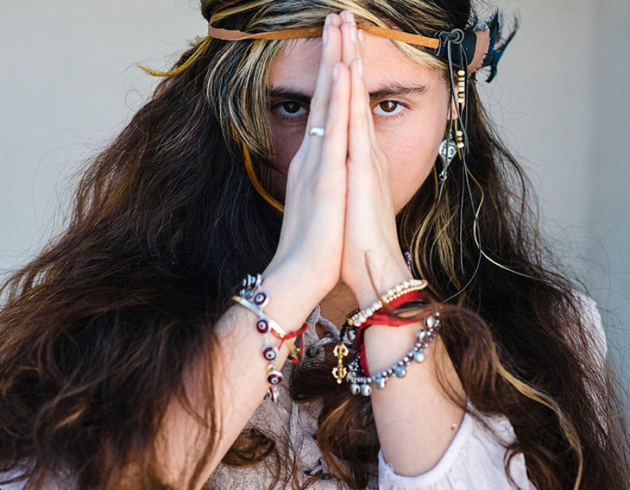 Close-up of hippie woman standing in prayer pose against wall