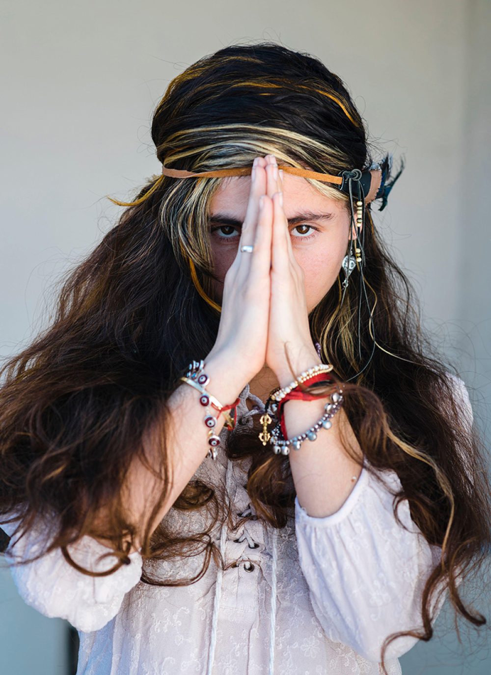 Close-up of hippie woman standing in prayer pose against wall